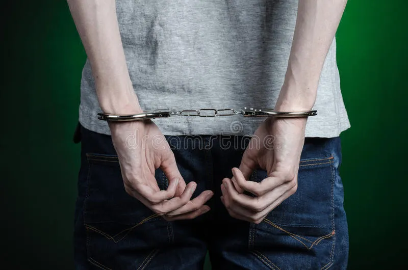 prisión-y-tema-condenado-hombre-con-las-esposas-en-sus-manos-en-una-camiseta-gris-y-tejanos-en-un-fondo-verde-oscuro-en-el-stu-54945967